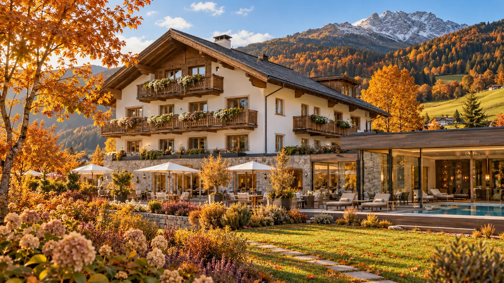 Das Hotel im Herbst: goldene Bäume, Abendsonne auf der Fassade, dahinter ein Gipfel mit erstem Schnee